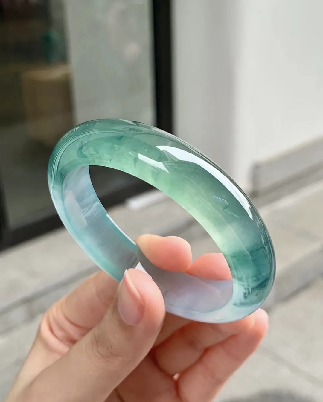 Translucent green jadeite bangle held in natural daylight